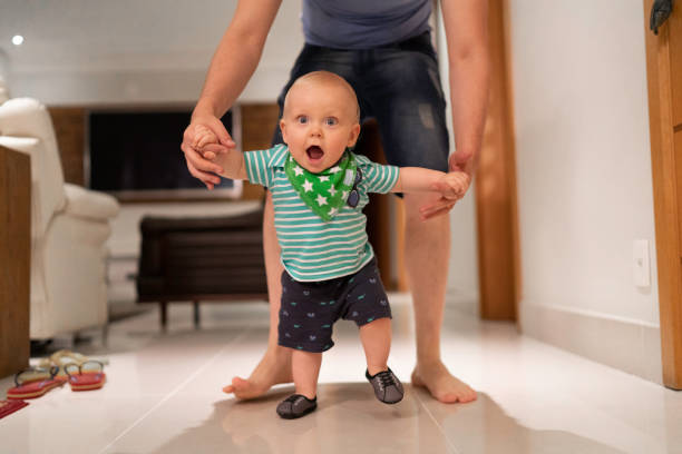 息子が家で歩くことを学ぶのを手伝う父 - 生後6ヶ月から11ヶ月 ストックフォトと画像
