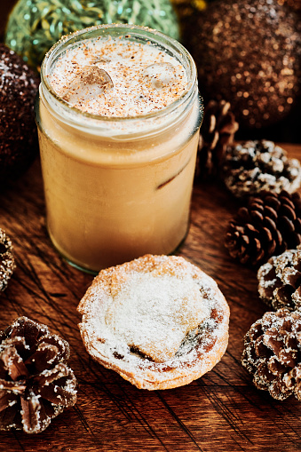 Iced festive Latte topped with cold milk foam and grated nutmeg, surrounded by christmas decorations, served with a Mince Pie.