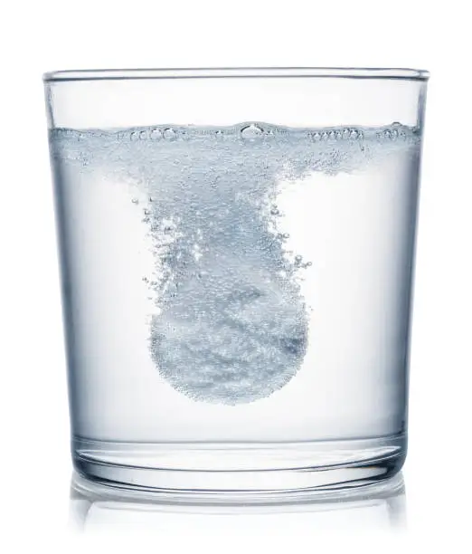Photo of Effervescent tablet dissolving in a glass of water. Clipping path.