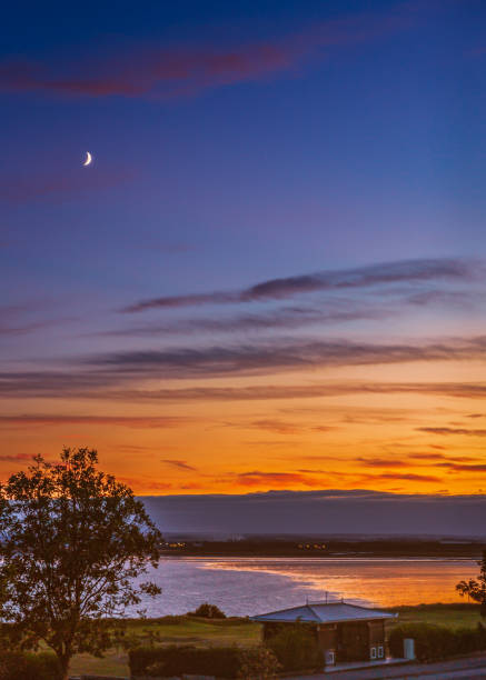 A new moon above Sandwich Bay as the golden sunset reflects into the low tide of the bay. A new moon above Sandwich Bay as the golden sunset reflects into the low tide of the bay. sandwich kent stock pictures, royalty-free photos & images