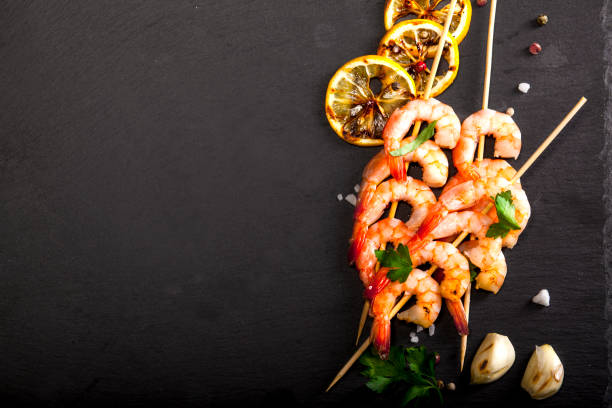 Prawns Shrimps with lemon, garlic and herbs on black background. Top view with copy space.