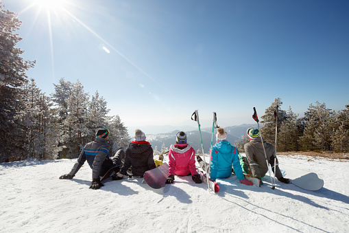 Skiers sitting on snow and looking landscape on skiing in mountain, back viewSki collage on mountain