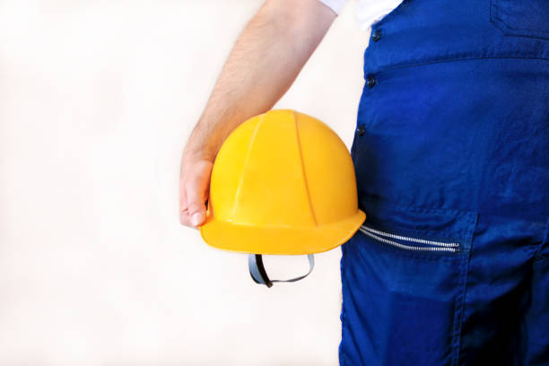 Construction worker and handyman is working on renovation of apartment. Builder at construction site with protective uniform and equipment, he with suit, coverall and yellow helmet holding in hand.