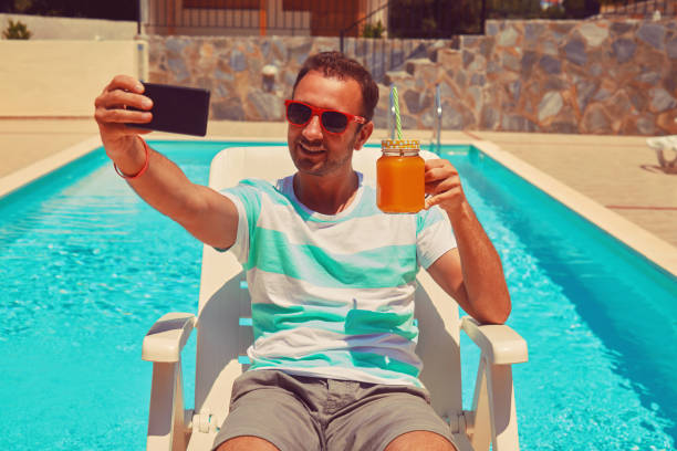 istock Attractive man using cellphone while drinking juice near swimming pool. 1173595300