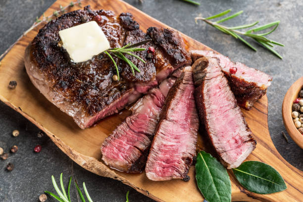 Medium rare Ribeye steak with herbs and a piece of butter on the wooden tray. Medium rare Ribeye steak with herbs and a piece of butter on the wooden tray. fork silverware table knife fine dining stock pictures, royalty-free photos & images