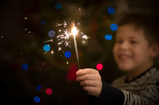 Closeup of a sparkler in hands of a happy kid boy. Christmas and Happy New Year celebration. Holidays season. Selective focus