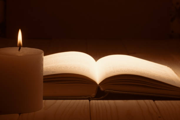 istock Open book with a candlelight on a wooden table 1173605314