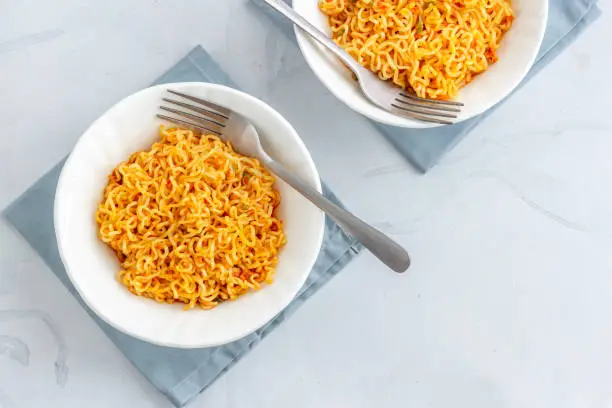 Two Bowls of Instant Noodles with Fork on White Background Directly Above Photo.