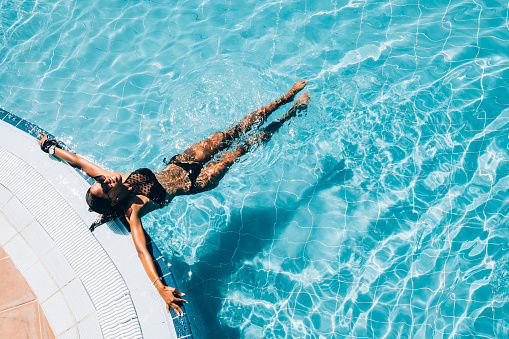 Millennial Black woman at  summer resort pool. She is enjoying her  summer vacation in Caribbean.