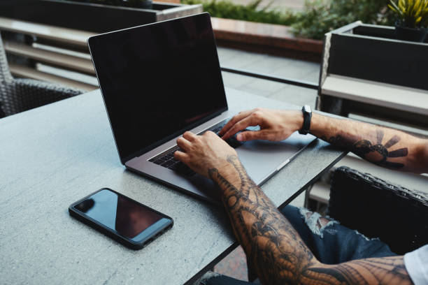 istock Young tattooed man working on laptop in cafe. Back view of human hands with tattoo using laptop at coworking office desk. Handsome guy typing text on laptop with blank copy space screen mockup 1173614010
