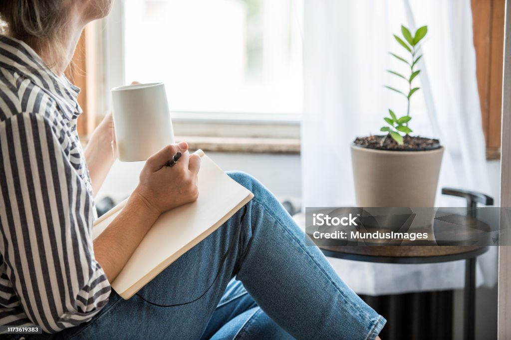 A young woman taking a break from technology A young woman takes a break to do something analog like writing in her journal and drinking tea. This is a healthy practice for those who experience anxiety. Writing - Activity Stock Photo