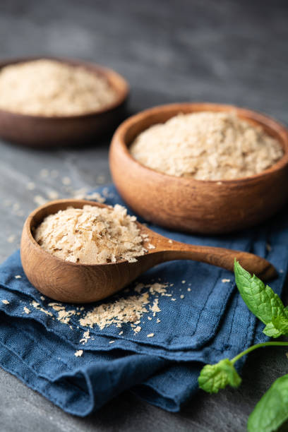 Dietary supplement, unfortified nutritional yeast flakes in a wooden bowl and scoop stock photo