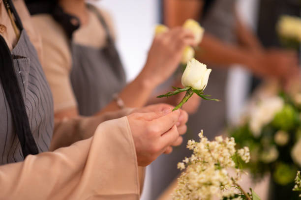 Midsection of florist removing white rose petal. Female is arranging flower. She is at floral training class.