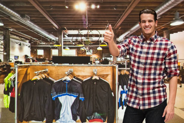 one man only / waist up / front view of 20-29 years old adult handsome people caucasian male / young men craftsperson / entrepreneur / manager / owner / sales clerk / sales occupation at the bicycle shop in front of merchandise with mountain bike - sales clerk store manual worker retail imagens e fotografias de stock