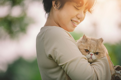 an asian chinese female teenager girl hugging her pet cat at public park in the morning