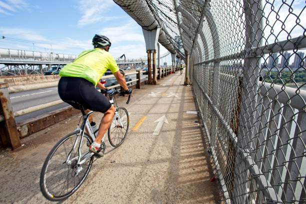 Bicycle rider on the George Washington Bridge bike and walkway heading to NYC Fort Lee, NJ, USA – September 8, 2019: Bicycle lane and walkway on George Washington Bridge accommodates a bicyclist on the way to NYC. Notice the suicide prevention fencing along the way. gwb stock pictures, royalty-free photos & images
