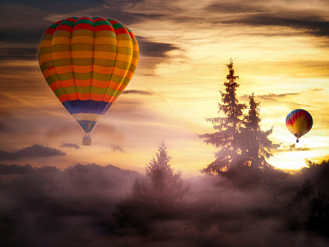 Hot-air balloon ride at sunrise in a fairytale-like landscape with wafts of fog