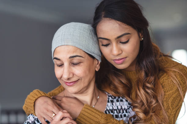 Courageous woman with cancer spends precious time with adult daughter A mature adult woman of Indian descent is spending time with her adult daughter. They are embracing. The daughter is resting her forehead on her mother's. They are smiling softly and have contemplative expressions. ovarian cancer stock pictures, royalty-free photos & images