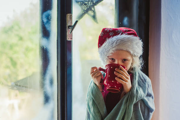 istock lovely child in christmas hat by the window 1173648740