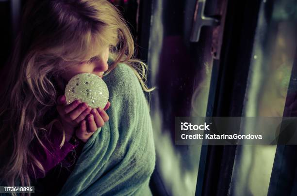 Child With Christmas Bauble Looking Through Window Stock Photo - Download Image Now - Sadness, Teenage Girls, Christmas