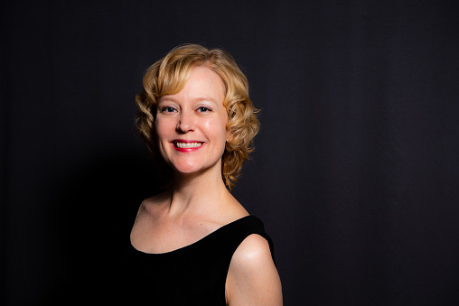 Studio portrait of a woman with short blond hair against a dark background.