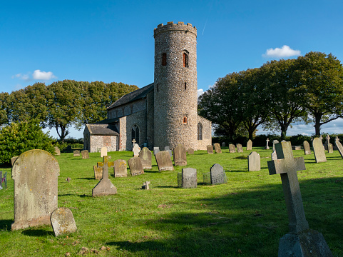 The medieval St Margaret's church and churchyard in Burnham Norton, Norfolk, Eastern England, on a sunny September day. The round Saxon tower is the oldest part, built at the end of the 11th century, and the remainder of the church was constructed over the following centuries: it is Grade I listed.