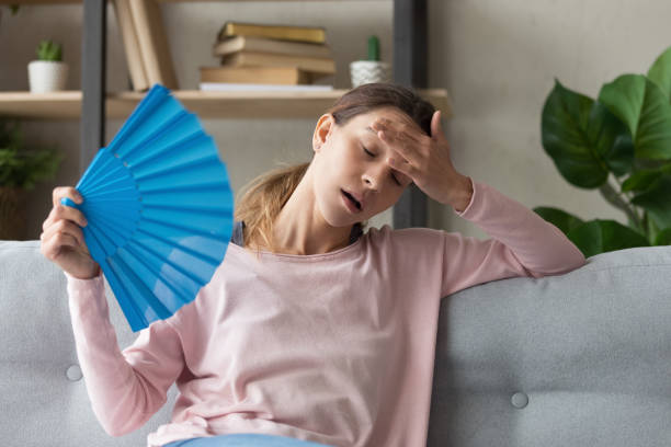 Overheated girl using hand waver suffering from heat Overheated millennial woman sit on couch at home feel warm waving with hand fan cooling down, sweating girl relax on sofa in living room hold waver suffer from heat, no air conditioner system overheated photos stock pictures, royalty-free photos & images