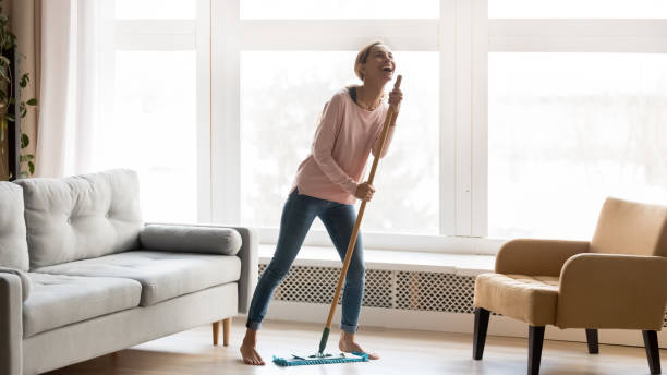 Happy young woman have fun dancing cleaning home Carefree happy young woman cleaning house living room have fun dancing with mop, smiling overjoyed millennial girl feel excited enjoy making home chores sing entertain using floor broom or Swiffer mop photos stock pictures, royalty-free photos & images