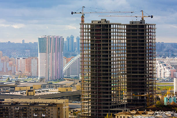Silhouettes of tower cranes in action on sunset. Preparing to pour a bucket of concrete into formwork. Construction a residential building. Small sharpness, possible granularity