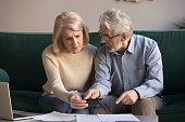 Serious stressed old couple looking at calculator feeling worried
