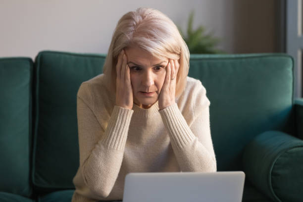 ショックを受けた成熟した女性は信じられないほどのオンラインニュースを読んでストレスを感じる - frustration emotional stress surprise women ストックフォトと画像