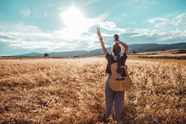 Casual dressed young woman with a guitar in the agricultural field on a sunny summer day