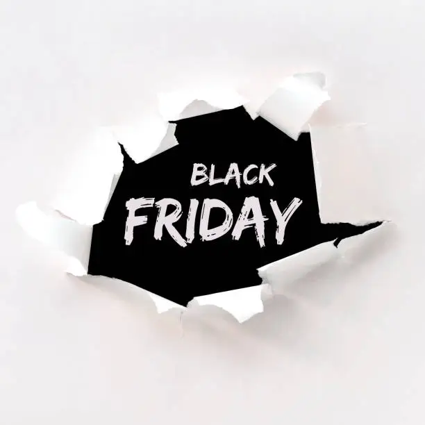 Photo of Black friday text in paper hole teared in white paper over black background