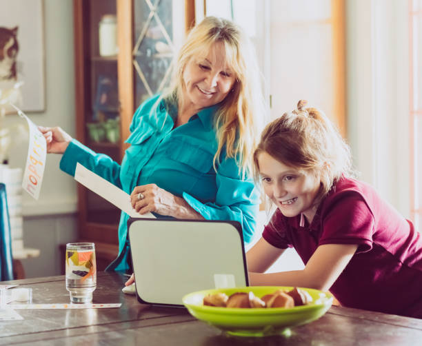 grandmother and elementary age child in a family dining room with a computer - grandparent using computer laptop dining table imagens e fotografias de stock