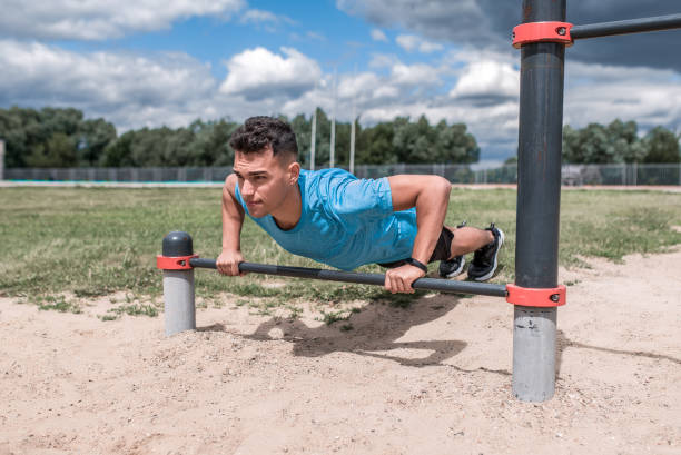 Male athlete does push-ups, fitness workout training, from crossbar in summer in city. Sportswear Sneakers Shorts. Active lifestyle young people, powerful stylish man. Strength motivation motion atleta masculino hace flexiones, entrenamiento de entrenamiento de fitness, de travesaño en verano en la ciudad. pantalones cortos deportivos. jóvenes de estilo de vida activo, hombre con estilo poderoso. movimiento de motivación de fuerza.