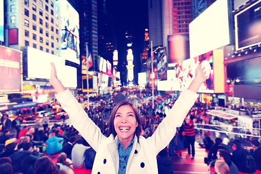 Success and fun- Happy excited woman in New York City, Manhattan, Times Square cheering celebrating joyful with arms raised. Cheerful Multiethnic Asian Caucasian young urban professional in her 20s.