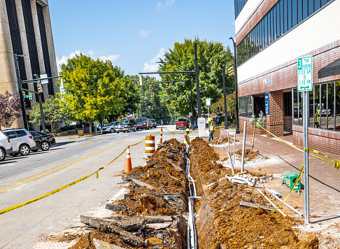 Hickory, NC, USA-3 Sept 2019: Workers laying underground cable in a ditch on a city street.