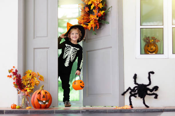 Kids trick or treat. Halloween. Child at door. Kids trick or treat on Halloween night. Child at decorated house door with autumn leaf wreath and pumpkin lantern. Little boy in witch and skeleton costume and hat with candy bucket. Fall decoration. candy house stock pictures, royalty-free photos & images