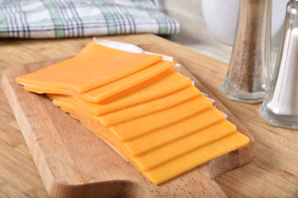 scheiben cheddar-käse auf einem schneidebrett - cheddar stock-fotos und bilder