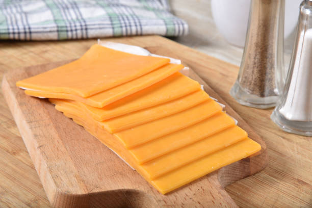 Slices of cheddar cheese on a cutting board Thick slices of cheddar cheese on a wooden cutting board cheddar cheese photos stock pictures, royalty-free photos & images