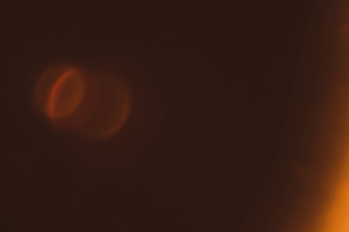 Defocused amber yellow lens flare. Brown abstract background. Light circles reflection effect.