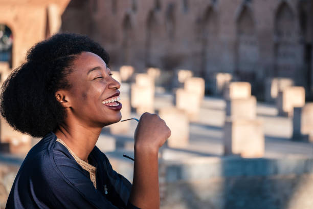 Shot of a young black woman outdoors holding sunglasses and laughing, in Marrakech, Morocco.