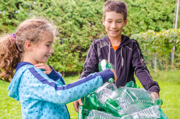 istock Boy and girl sitting beside a recycling bin 1173704848