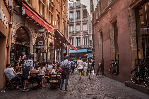Picture of a Bouchon restaurant seen from a nearby street of the vieux Lyon with waiters and clients standing. A bouchon is a type of restaurant found in Lyon, France, that serves traditional Lyonnaise cuisine
