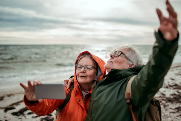 Seniors Selfie Close up of two female seniors taking a selfie by the beach raincoat photos stock pictures, royalty-free photos & images