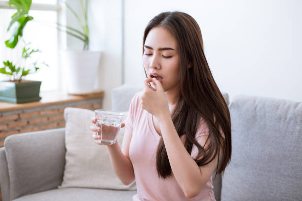 Sick young woman taking pills while sitting on the sofa at home stock photo