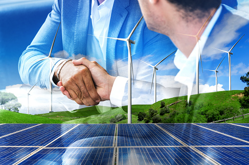 Double exposure graphic of business people handshake over wind turbine farm and green renewable energy worker interface. Concept of sustainability development by alternative energy.