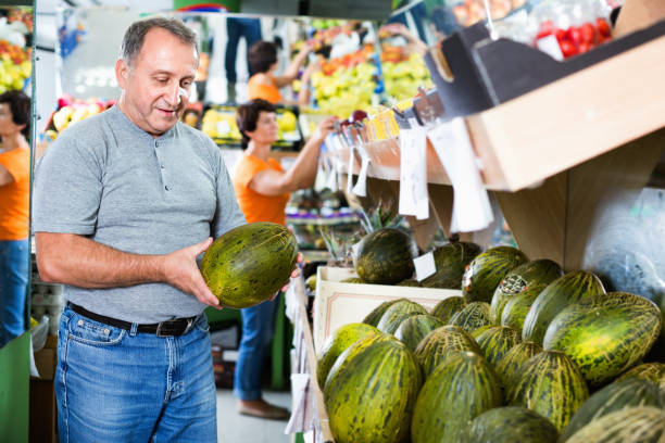 Smiling male is choosing green melon in the supermarket.