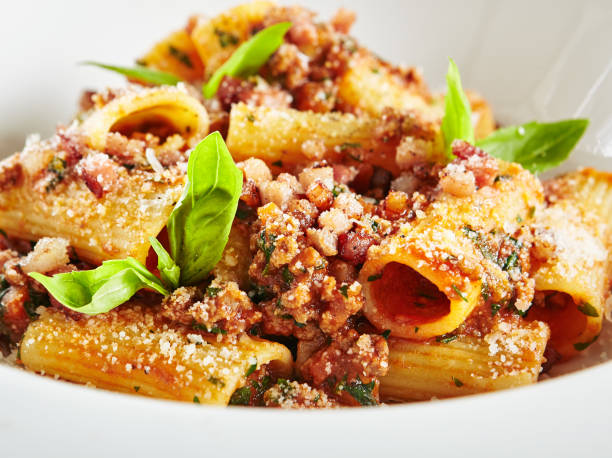 Homemade Rigatoni with Bolognese Sauce and Smoked Pork Belly Exquisite Serving White Restaurant Plate of Homemade Rigatoni with Bolognese Sauce and Smoked Pork Belly Close Up. Stylish High Kitchen Italian Penne Pasta Tubes on Natural Black Marble Background rigatoni stock pictures, royalty-free photos & images