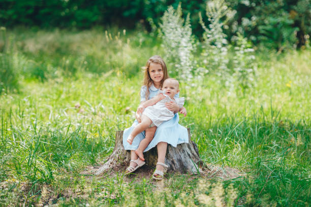 istock Two cute young sisters sitting on stumps with green meadow on background 1173737423
